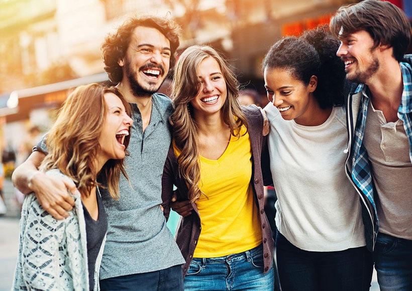 Group of smiling friends with arms around each other outdoors