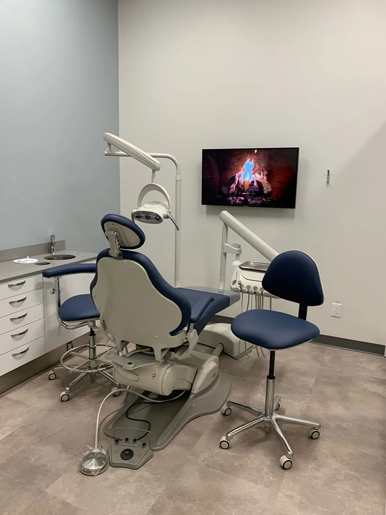 Modern dental operatory at Allard Station Dental with a comfortable navy chair and a wall-mounted fireplace video for patient relaxation